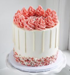 a white cake with pink frosting and sprinkles on top sitting in front of a window