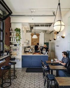 people sitting at tables in a restaurant with blue cabinets and white walls, while one person works on his laptop