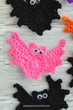 crocheted bats with googly eyes are on a white surface and one is black, the other is pink