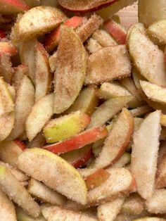 sliced apples are sitting in a pile on a wooden table with sugar sprinkled on them