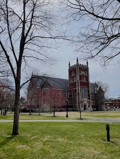 a large red building surrounded by trees in the middle of a green field with no leaves on it