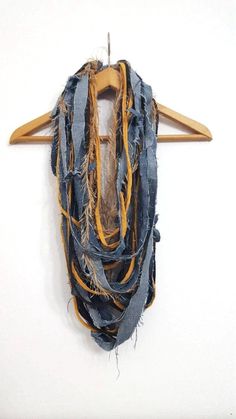 a piece of clothing hanging on a wooden hanger next to a white wall with a blue and yellow scarf draped over it