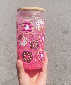 a hand holding a pink glittered cup with donuts and sprinkles on it