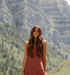 a woman standing in front of a mountain with her hands on her hips and looking at the camera