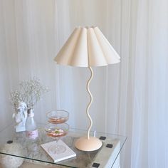 a glass table topped with a lamp next to a vase filled with flowers and other items