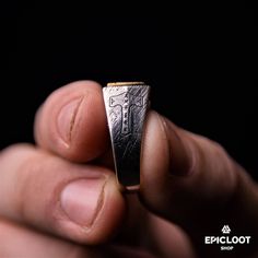 a hand holding a silver ring with a cross on the front and side, against a black background