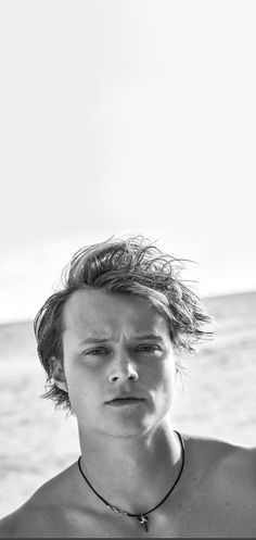 black and white photograph of a man with no shirt on standing in front of the ocean