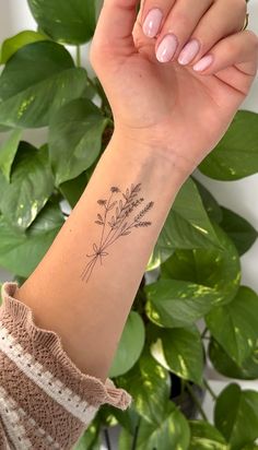 a woman's arm with a small tattoo on it, and a plant in the background