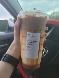 a person holding up a cup of iced coffee in their hand while sitting in a car