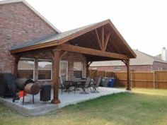 a covered patio with grills and chairs in front of a brick house on a sunny day