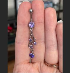 a person holding a purple and silver navel ring