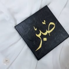 an arabic calligraphy on a black and gold painted piece of art with white sheets