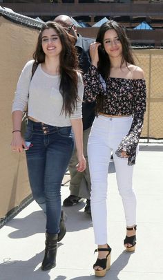 two women walking down the street together, one wearing white pants and black heels with her hand in her pocket