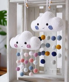 two crocheted cloud mobiles hanging from strings in a white frame with multicolored balls