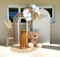 a teddy bear sitting in front of a baby's gate with balloons on it