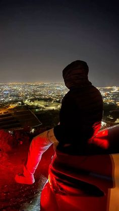 a person sitting on top of a car looking out over the city lights at night