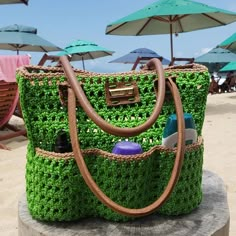 a bag made out of grass on the beach with umbrellas in the back ground