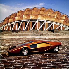 an unusual looking car parked in front of a large wooden structure on top of a brick floor