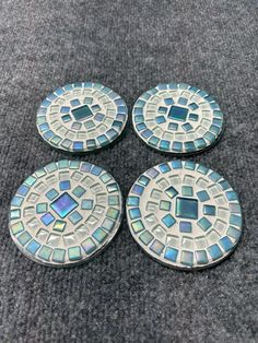 four blue and white mosaic tile coasters sitting on top of a gray carpeted floor