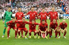 a group of men in red soccer uniforms posing for a team photo on the field