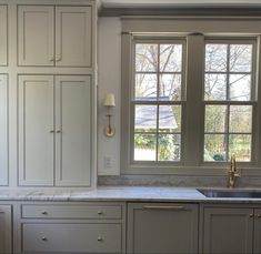 a kitchen with white cabinets and marble counter tops, along with two windows that look out onto the yard