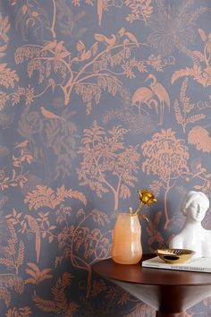 an orange vase sitting on top of a table next to a wallpapered wall