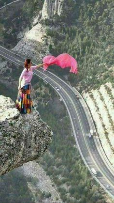 a woman standing on the edge of a cliff holding an umbrella