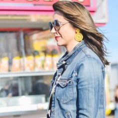 a woman wearing sunglasses and a denim jacket is standing in front of a food stand