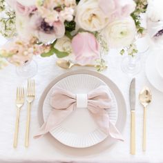 the table is set with white plates, silverware and pink flowers