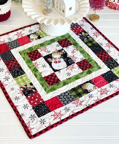 a quilted table runner with a house on it and christmas decorations around the edge