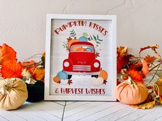 a red truck with pumpkins and leaves around it on a white table next to a sign that says pumpkin kisses & harvest wishes