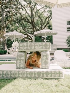 a woman laying on top of a bed in the middle of a yard with an umbrella over her head