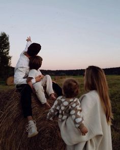 three people sitting on hay bales with one person reaching up to grab something from the other