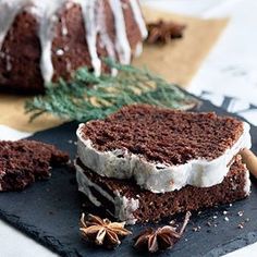 two slices of chocolate cake with icing on a slate board next to cinnamon sticks