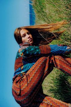 a woman with her hair in the air and wearing patterned clothing, leaning against a tree