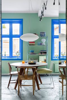 a dining room table with chairs and a lamp hanging from it's ceiling in front of blue windows