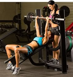 a woman is doing a bench press with another woman in the background holding a barbell