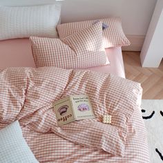 a bed covered in pink and white checkered sheets with a book on the pillow