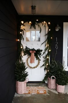 christmas wreaths and potted plants on the front door of a house with lights