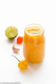 a jar filled with orange sauce next to a slice of lime and some chili peppers