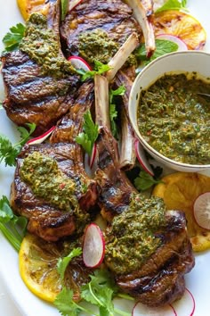 grilled lamb chops with pesto sauce and lemon slices on a white plate