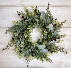 a green wreath with red berries and greenery hanging on a white wooden wall,