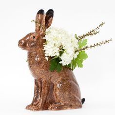 a ceramic rabbit with flowers in it's mouth sitting next to a white background