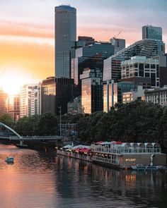 the sun is setting over a river with boats on it and tall buildings in the background