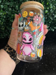 a hand holding a glass jar with stickers on it and plants in the background