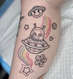 a tattoo on the leg of a person with an alien ship and rainbows in the background