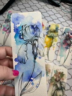 a person holding up some watercolor paper with flowers on it and another drawing in the background