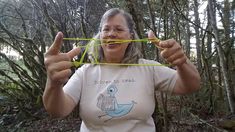 an older woman holding up some string in front of her face while standing in the woods