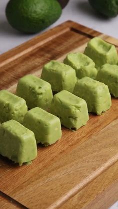 several pieces of green food on a cutting board with avocados in the background