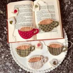 an open book sitting on top of a table next to two pieces of fabric in the shape of teacups